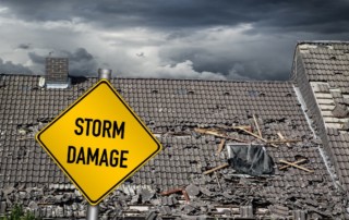 Yellow storm damage sign with damaged roof in background