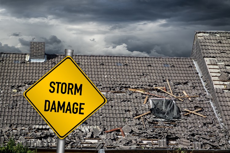 Yellow storm damage sign with damaged roof in background