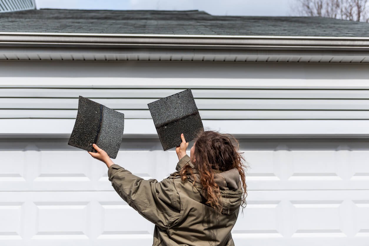 Woman holding up shingles trying to determine where they came from.