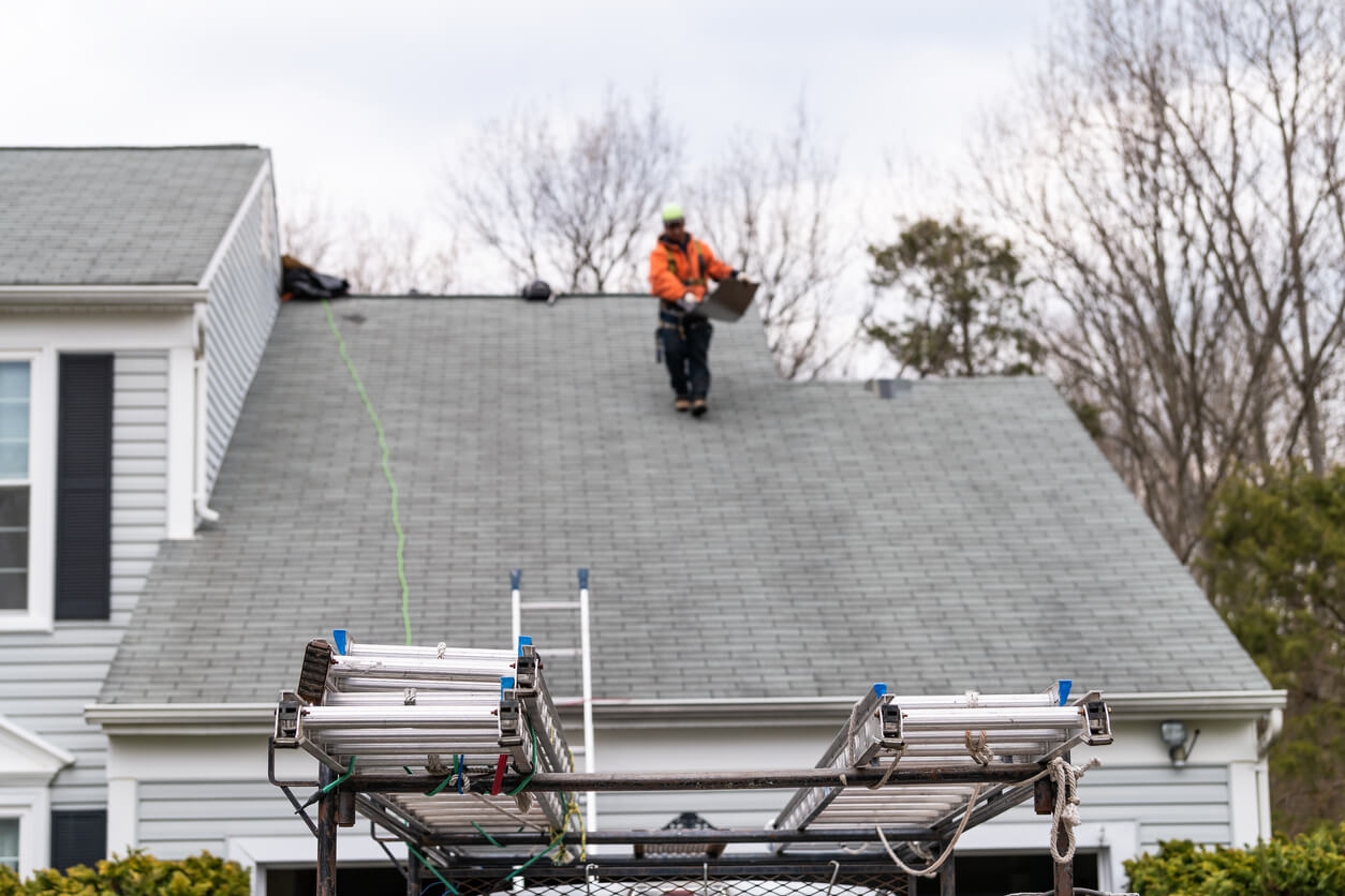 House during day over garage with truck, gray color Single Family Home and man walking on roof shingles and ladder during repair